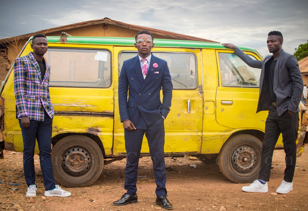 services-04 Three fashionable men in suits pose by a rustic yellow van in an outdoor setting.