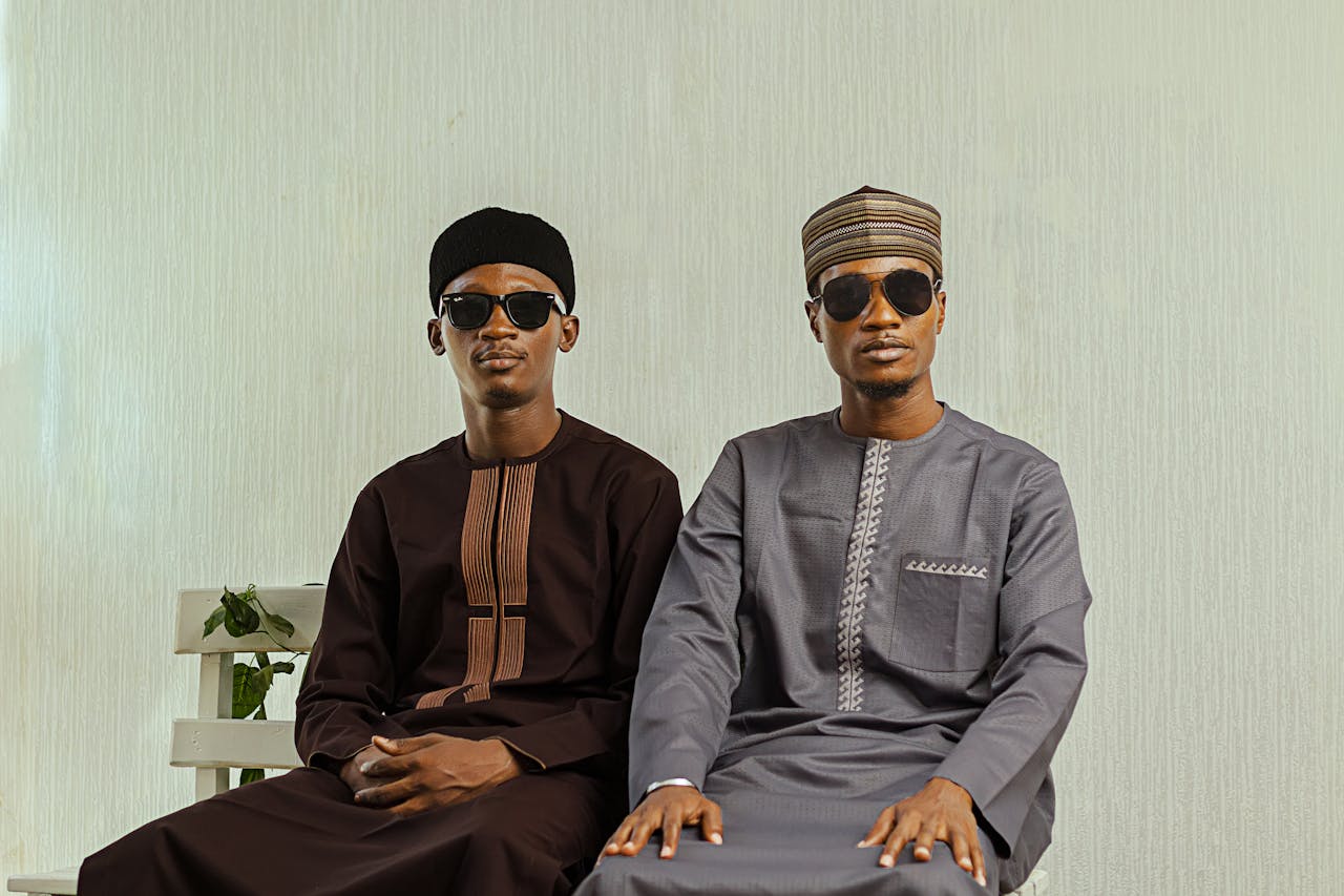 who-we-are Two men in sunglasses wearing traditional Nigerian attire indoors.